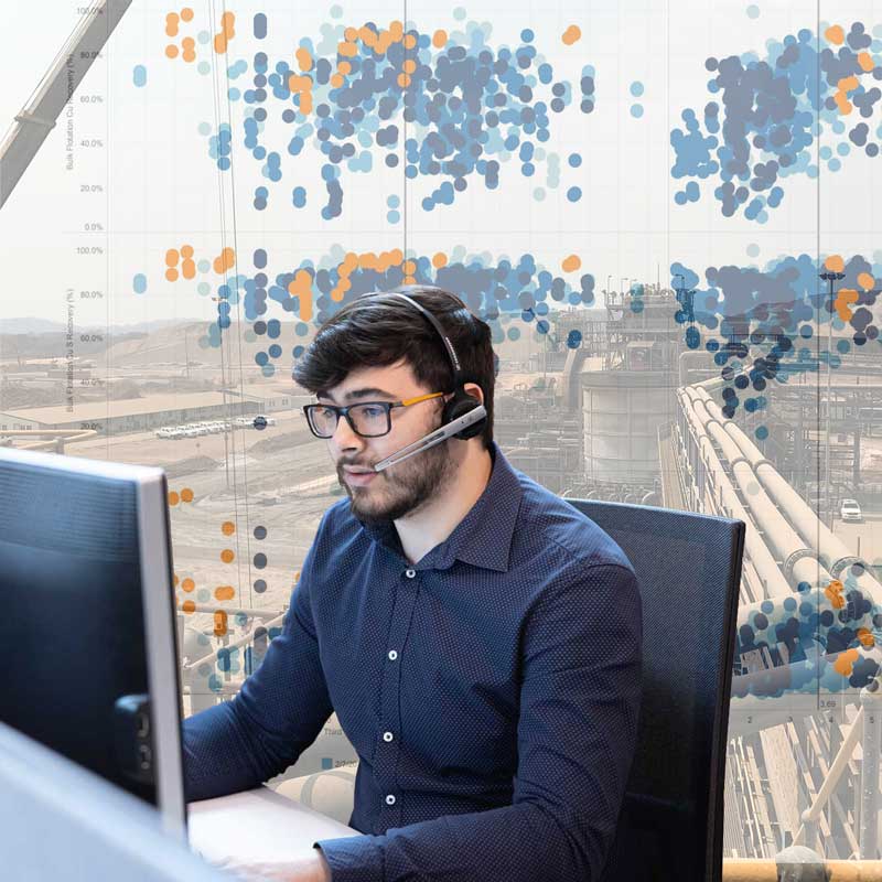 A Metallurgical Systems team member offers support infront of a backdrop of plant machinery overlayed with data reports from software