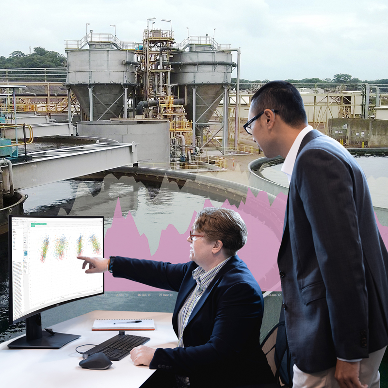 Metallurgical intelligence consultants analyse results on a monitor with a metallurgical plant in the distance