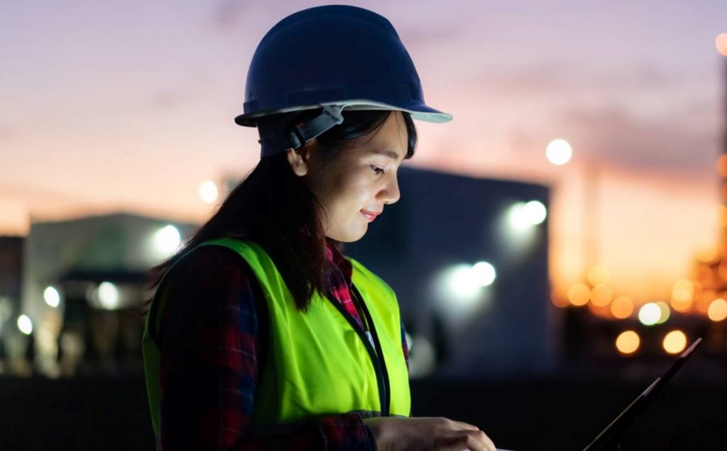 Worker in site gear on laptop at processing plant